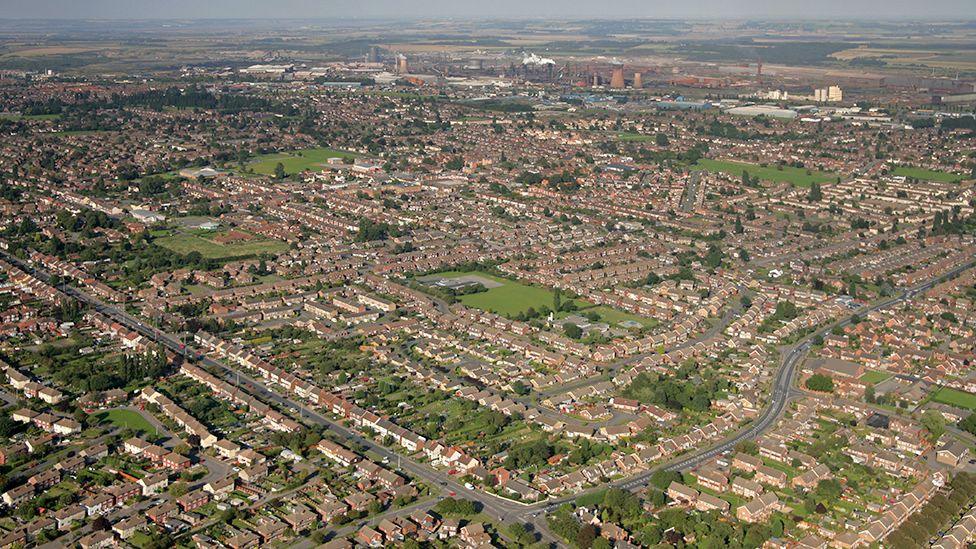 Aerial view of Scunthorpe showing rows of houses and parks with the steel works in the background