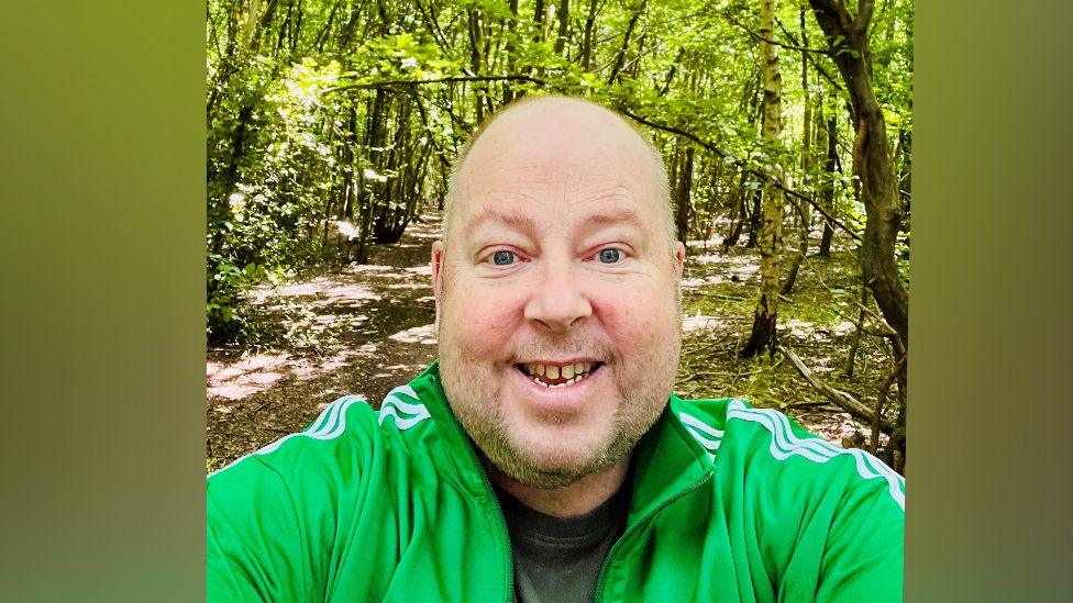 James Hillery photographed in a woodland wearing a bright green sports top and smiling at the camera