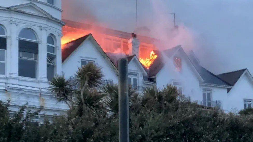 Large white building with pitched roofs and orange glow from flames in its centre 