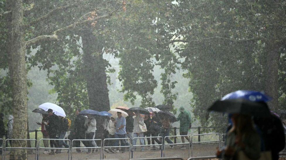 People walk with umbrellas as they're hit by rain and heavy winds