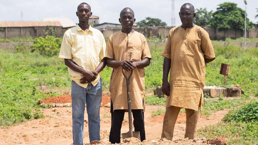 Magaji Abdullahi (C) with his hands rest on the handle of a spade standing in between his cousins and his two cousins Aliyu (L) and Abdullahi (R) at Tudun Wada graveyard in Kaduna state, Nigeria