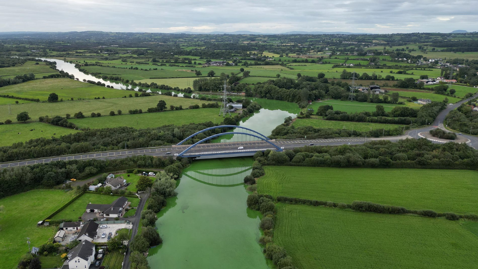 Drone shot showing green fields in Toome with bright green river flowing through it