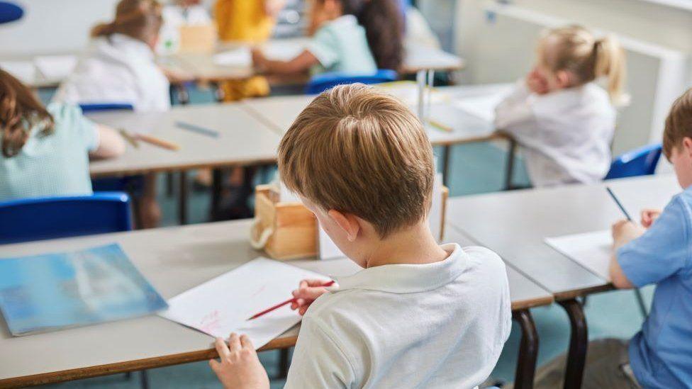 A school pupil faces away while sat at a desk writing