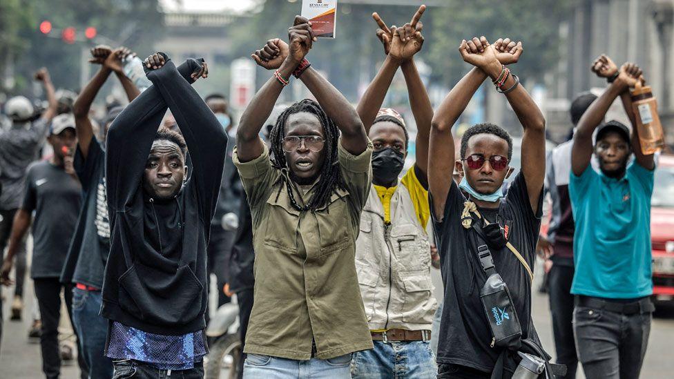 Protesters with arms aloft shout slogans at riot police during a protest to oppose a proposed Finance Bill 2024, in Nairobi, Kenya, 18 June 2024