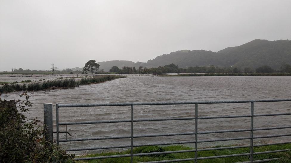 Water has completely covered a farmers field. The water stretches off across the whole of the field and stops just before a metal gate, leaving the scene looking like a giant lake.