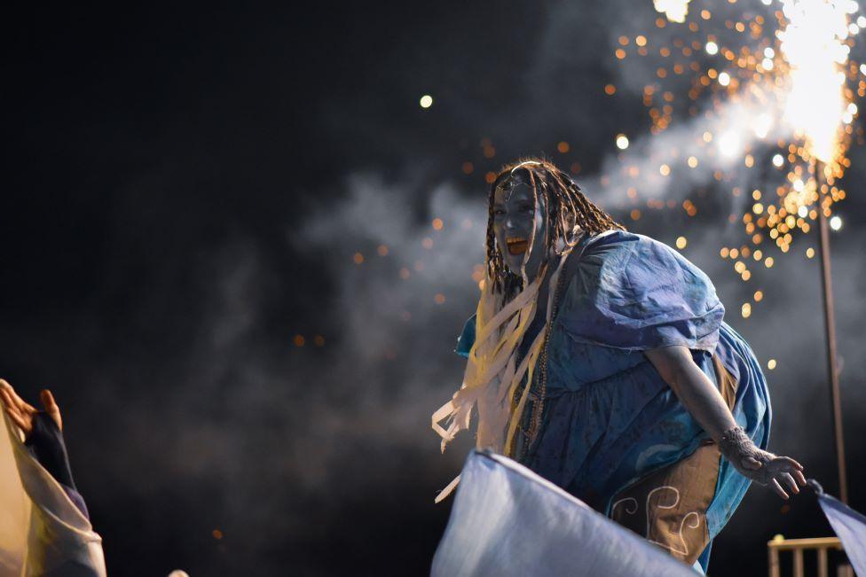 A woman dressed in blue costume with sparklers in the background.