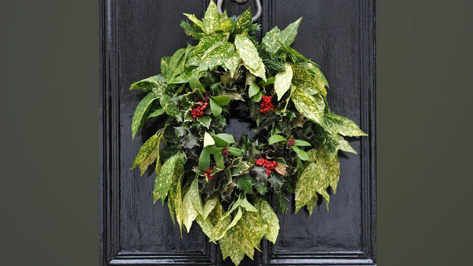 Christmas wreath hanging from a black front door, 2010. It has a ring of variegated leaves in lighter shades of green on the outside and an inner ring of dark green holly leaves with scarlet berries