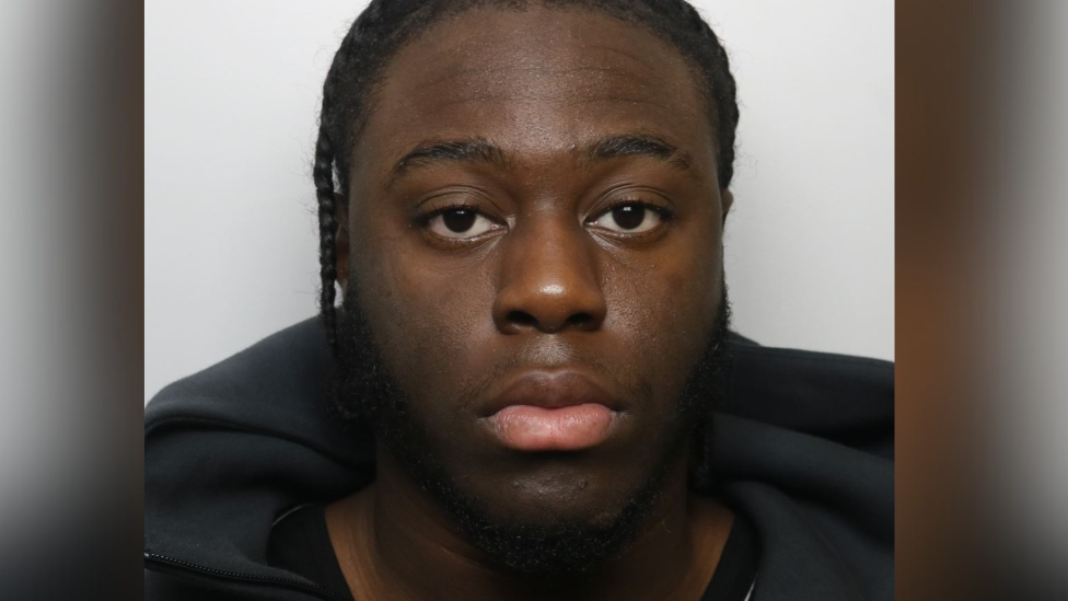 A police mugshot of Paul Hayden, wearing a black hoodie with his hair in cornrows.
