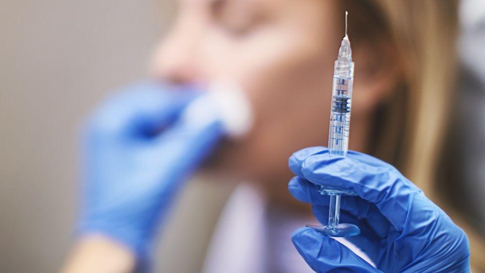 Picture of a medical needle with a woman's face in the background