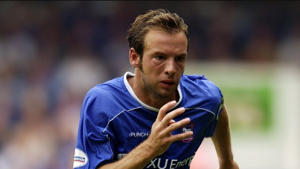 Marcus Stewart, pictured in the early 2000s in a head and shoulders image. He is playing for Ipswich Town, wearing their blue kit, with his right arm raised while running. He has short brown hair.