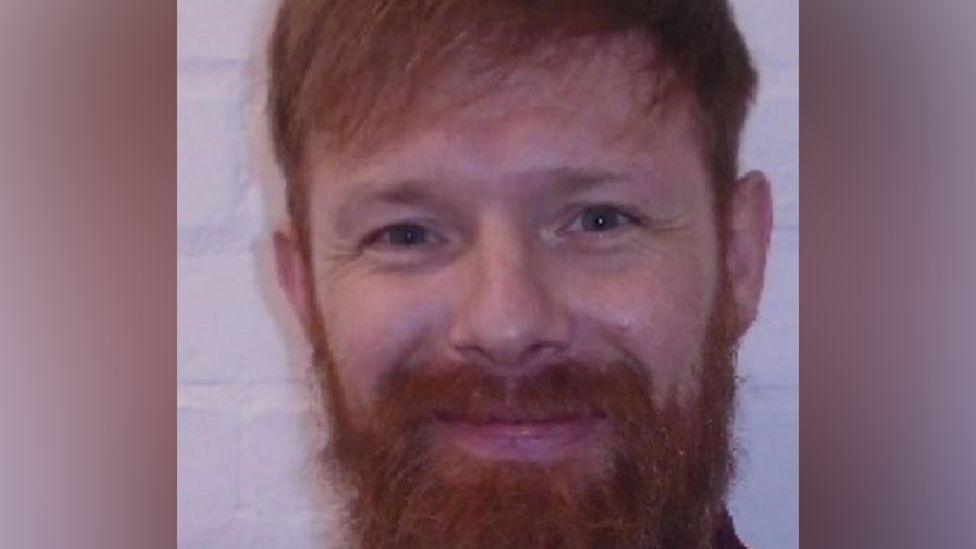 Michael Gilworth with a ginger beard and hair, in a police photo, looking straight at the camera. 