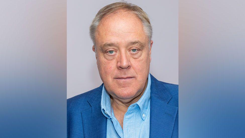 Richard Howitt wearing open necked blue shirt and a blue suit. He is looking directly at the camera.