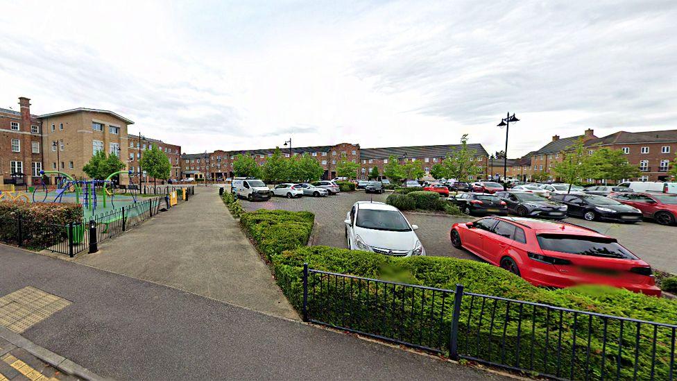 The centre of Shortstown, showing parked cars, new-build flats, a play area and footpath