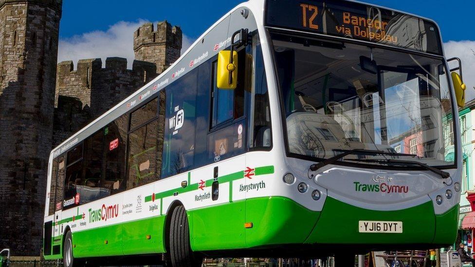 A TrawsCymru bus, whose sign says it is the T2 to Bangor via Dolgellau, pictured in front of a castle.