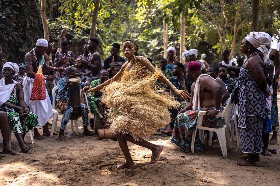 A Voodoo devotee dances during a festival surrounded by people in a forest 