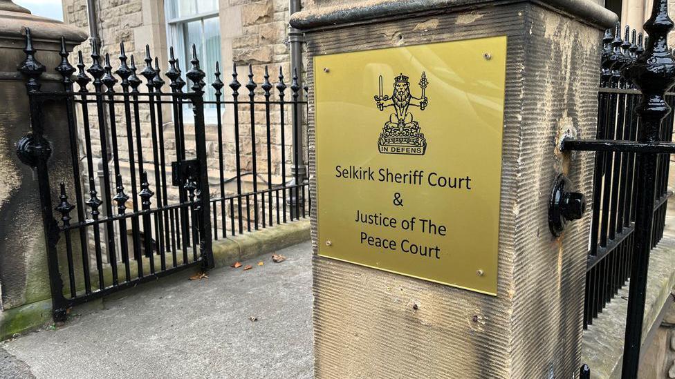 A sign saying Selkirk Sheriff Court and Justice of the Peace Court on a stone pillar beside railings and a gate