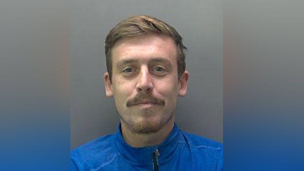 Police custody mugshot of James Heaney. He is wearing a blue top, moustache and beard.