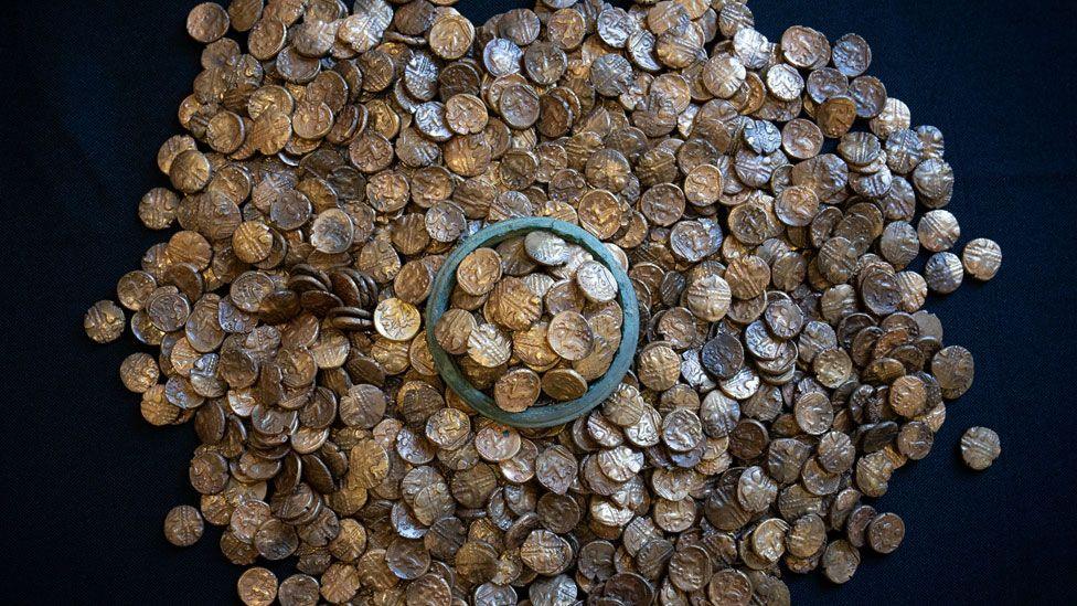 A pile of 933 Iron Age gold coins resting on a black background. In the middle coins are heaped around the rim of a vessel.