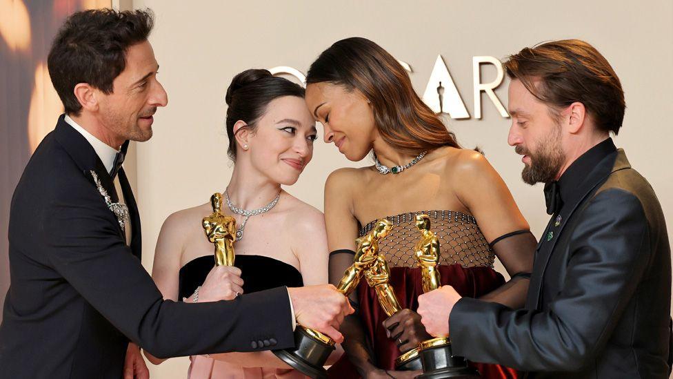 Adrien Brody, Mikey Madison, Zoe Saldana and Kieran Culkin standing together with their Oscars