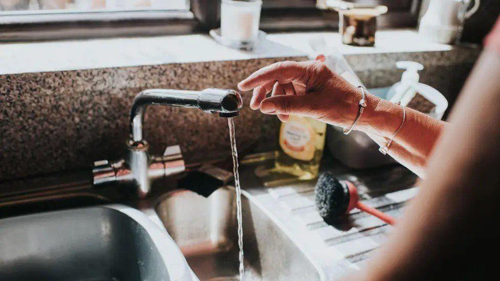 Tap with water running and a person's hand near the tap. 