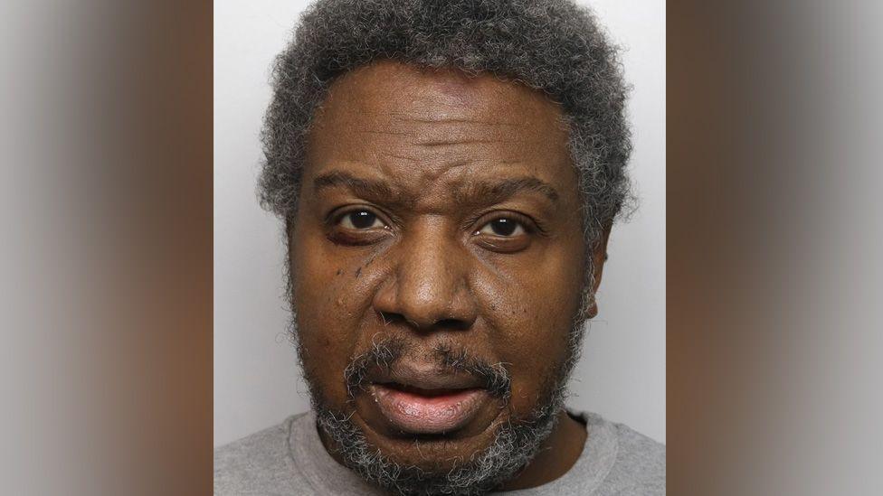 A custody image of Jazwell Brown. He is wearing a grey top and has short, greying hair and a grey beard.
