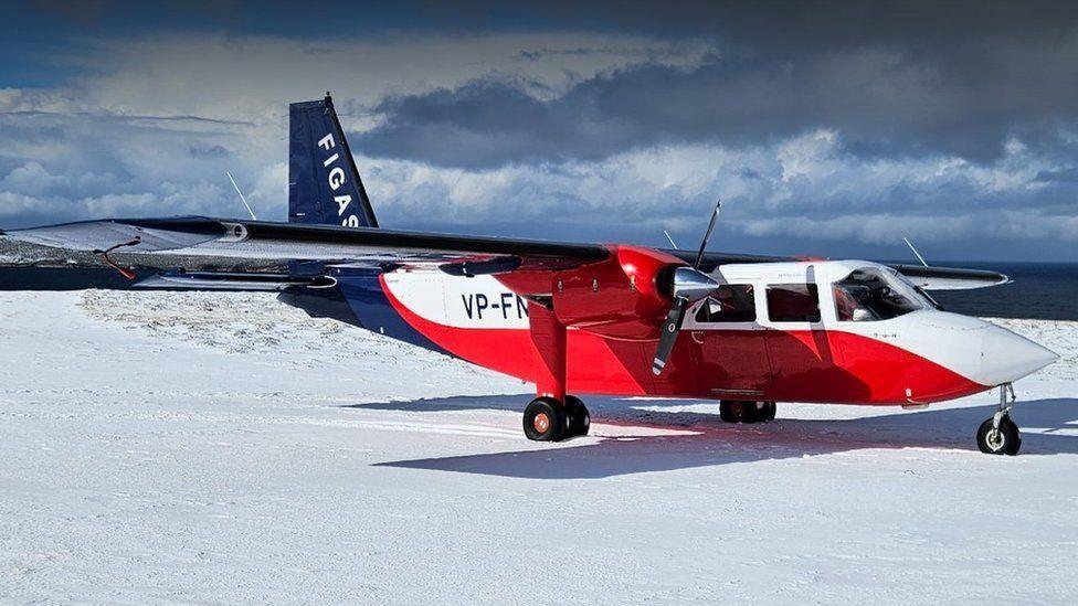 A red, blue and white aircraft on the snow-covered ground with its engines not running.