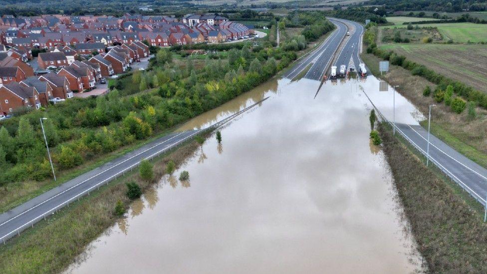 The A421 dual carriageway submerged in water, with tankers trying to pump it out. Shot from a drone.