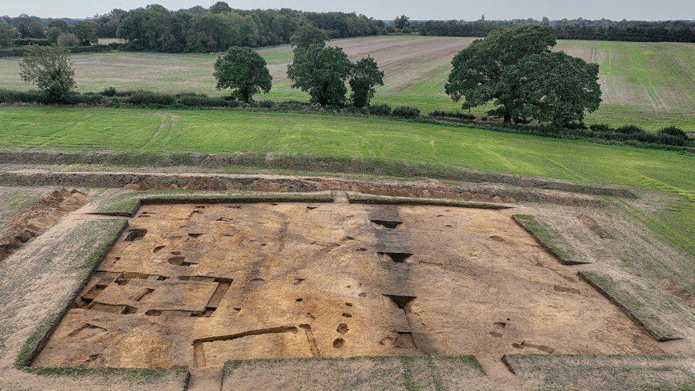 A drone image of a field that has been excavated to reveal the imprint of a large structure. Marks in the ground can be seen where the building once stood.