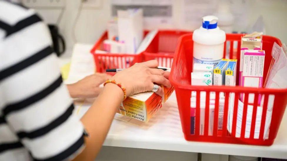 An image of someone's hands on some medicine in a pharmacy. The hands are sorting the medical supplies into red boxes.