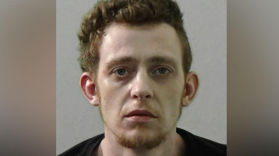 Mugshot of Reece Galbraith. He has thick ginger hair and a ginger goatee and a very pale face. He is wearing a black t shirt.