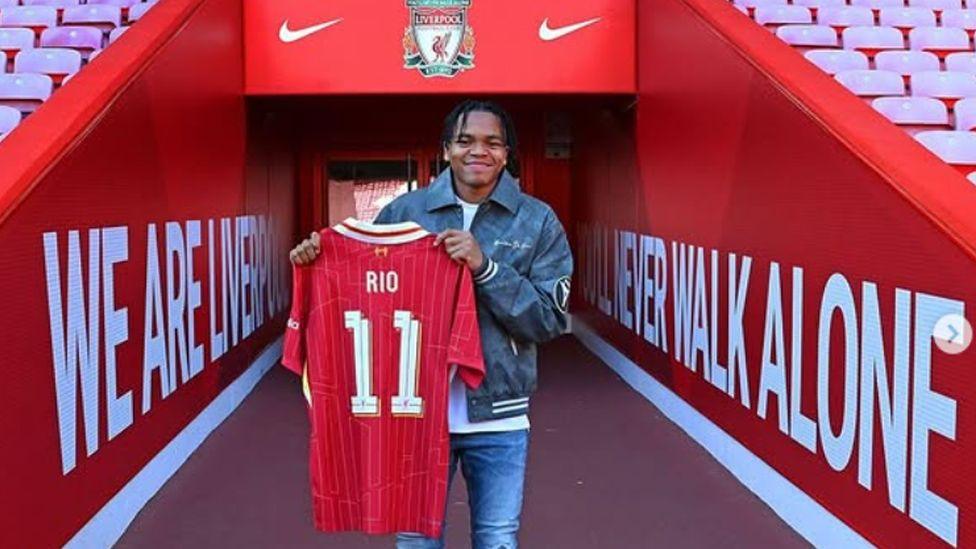 Rio Ngumoha holding a Liverpool shirt after signing with the team in 2024.
