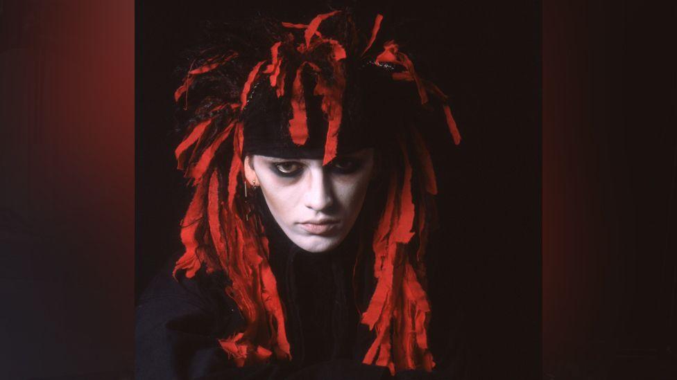 A young Pete Burns in red and black headwear with white face and dark eye make up