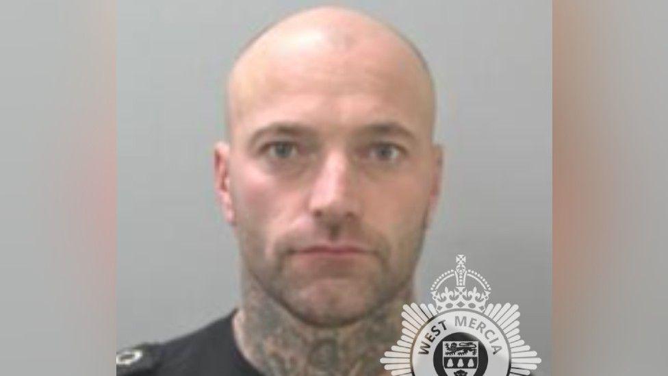 A mug shot of a bald man who has tattoos on his neck. He is staring into the camera with a straight face. Half of the West Mercia Police logo is visible at the bottom of the mug shot. 