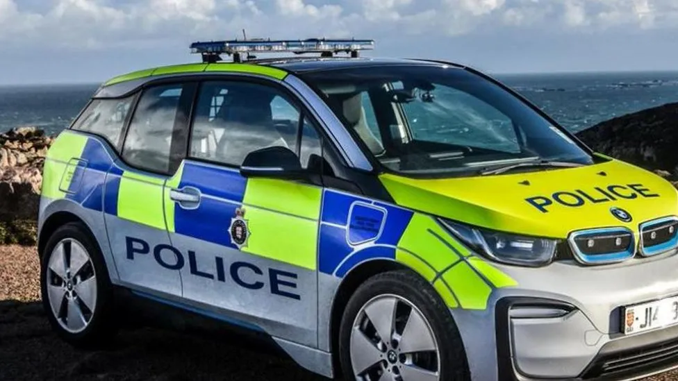 A Jersey police car in blue and yellow livery parked near the coast with the sea behind