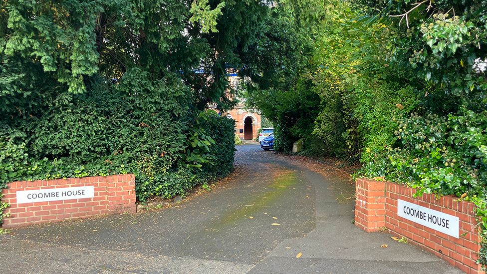 Entrance of Coombe House. Signs on low balls either side of the long drive lead up to the main building, which is hidden by trees and shrubs