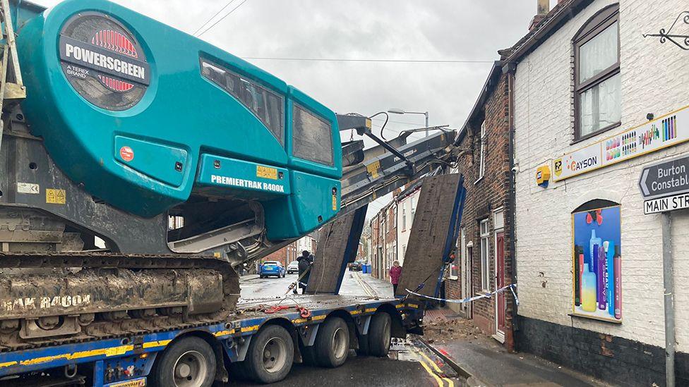 The scene of the crash showing a blue Premiertrak R400 Jaw crusher on the back of a trailer which has apparently hit the top floor of a redbrick terrace house