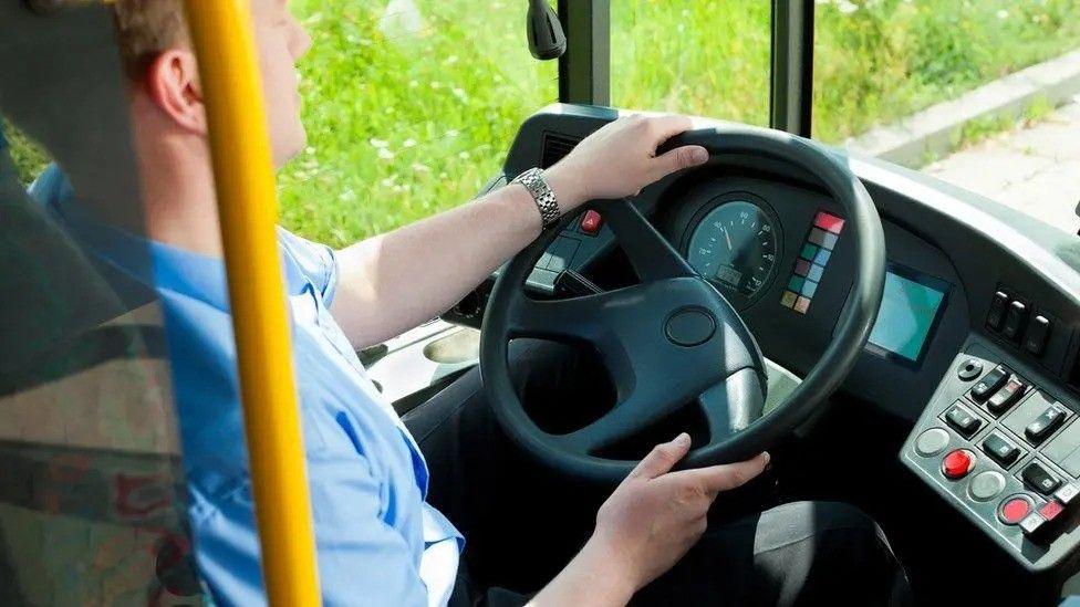 A view of a male driver steering the wheel of a bus on a sunny day.
