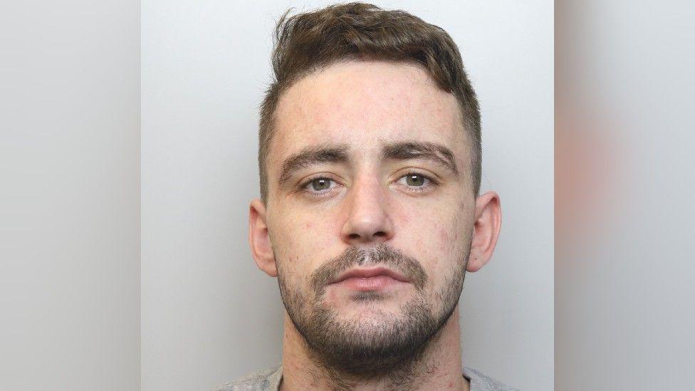 Police mugshot of Daniel Carter who has short dark hair and dark stubble.