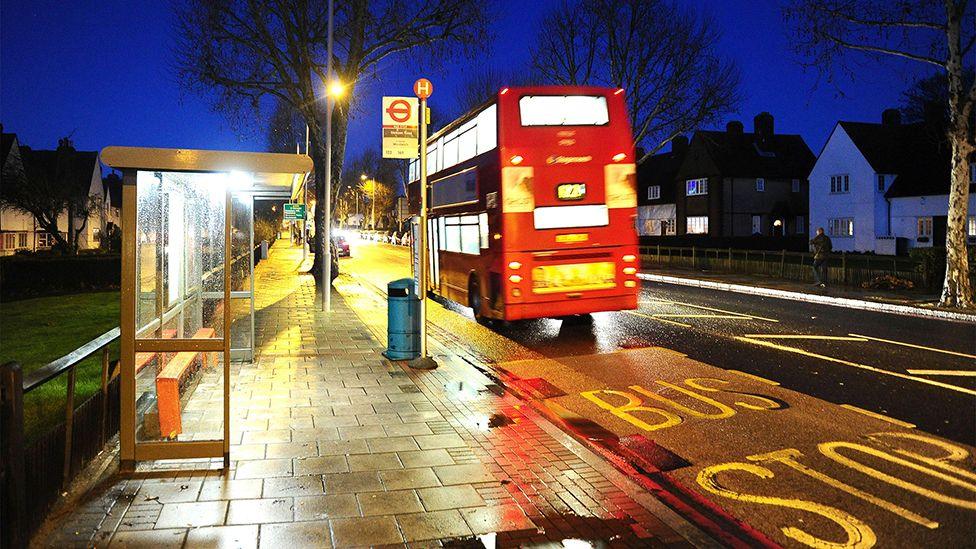 Bus passing bus stop in Eltham at night