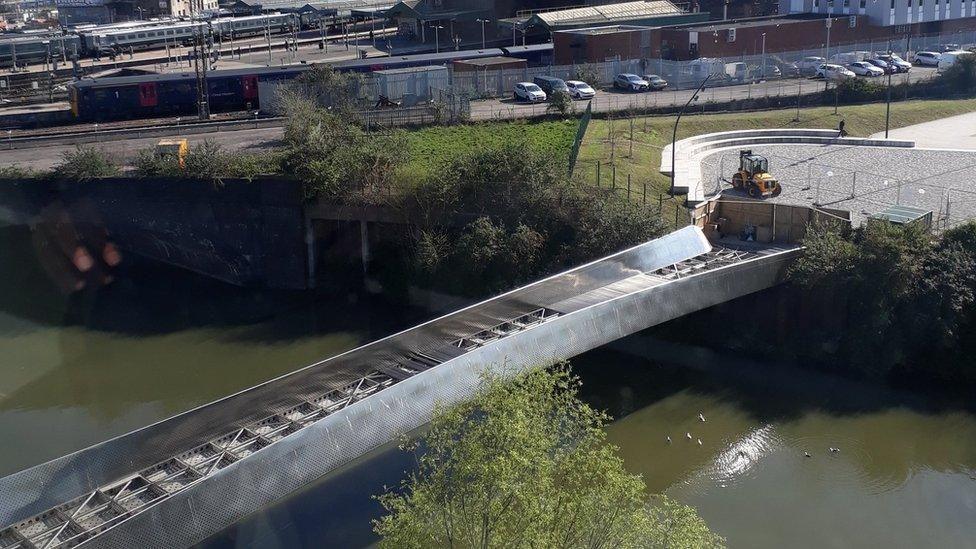 An aerial image showing the metal bridge over a brown-green river. The deck panels have been lifted during resurfacing work. In the background you can see trains on the track at Temple Meads Station.