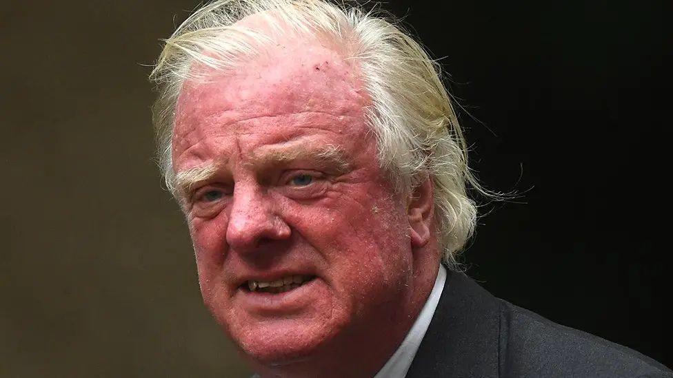 Head and shoulders shot of MP Edward Leigh. He is wearing a white shirt and grey suit jacket and is looking past the position of the camera.