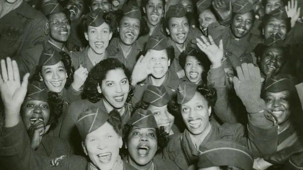 Members of the 6888th Central Postal Directory Battalion look towards the camera and smile and wave