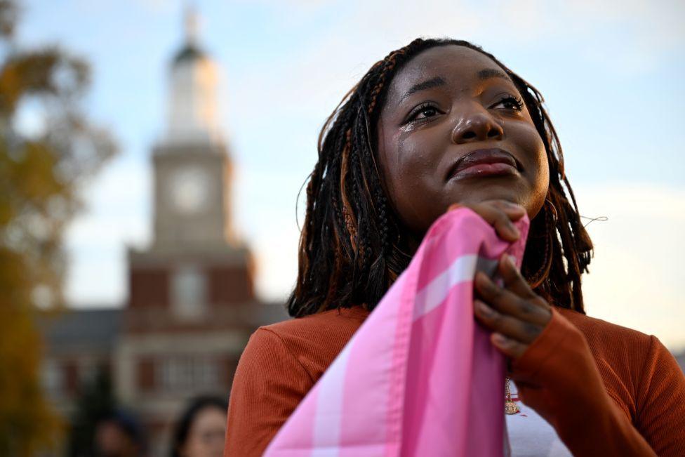 An African American woman holds a flag and looks tearful as she listens to Democratic presidential nominee Kamala Harris concede the election during a speech at Howard University