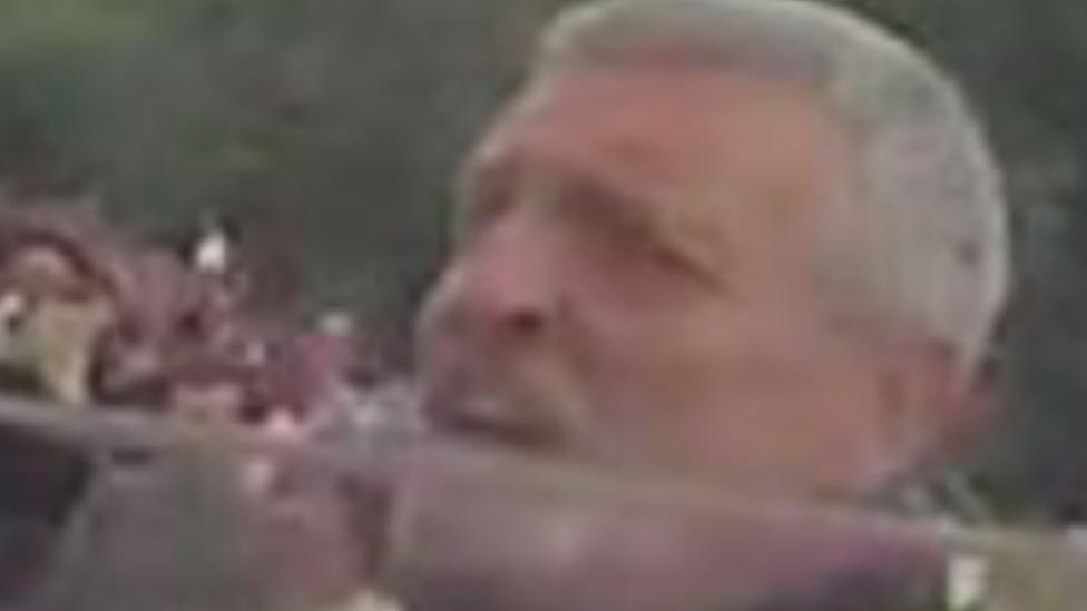 A man with grey hair looking angry in a crowd of people 