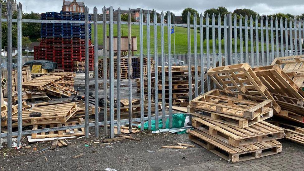 pallets and other materials for a bonfire seen through a hole in iron railings