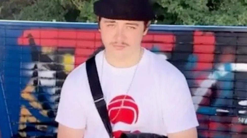 Raymond James Quigley looking directly at the camera wearing a black hat and red and white T-shirt