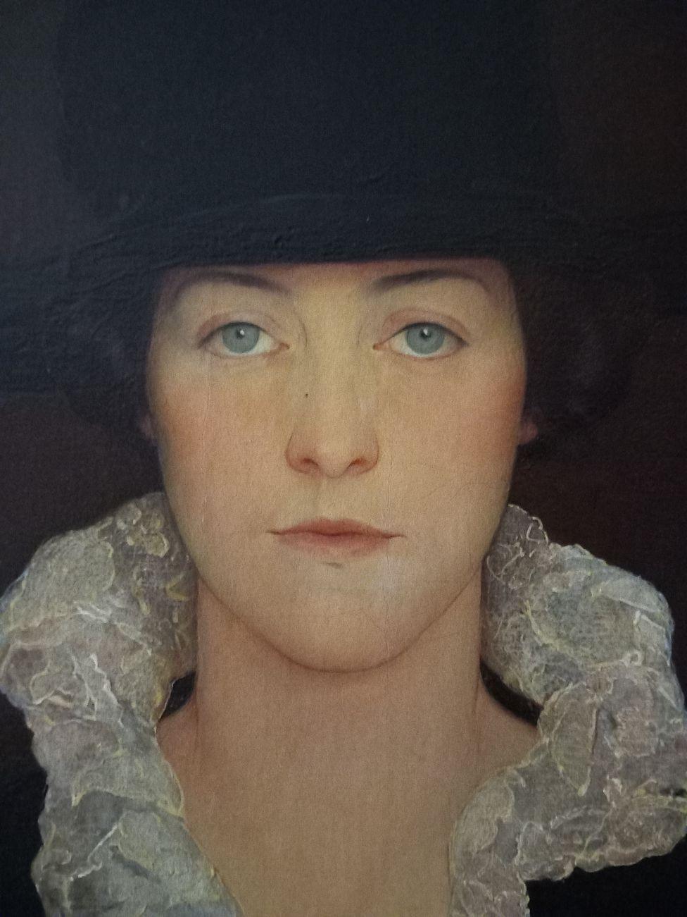 An oil painting of Dorothy dressed in a black dress with a large lace, white collar. The paint is reminiscent of Pilgrim dress and features a large talk black hat. She stares sternly out from the portrait.