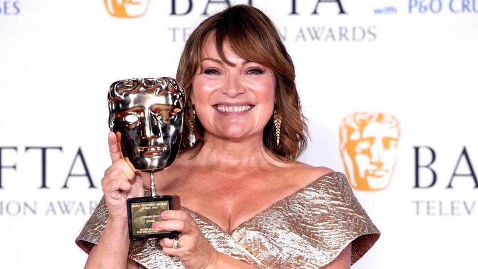 Lorraine Kelly smiling broadly at the camera, while holding a BAFTA in her hands. The white background says BAFTA Television Awards