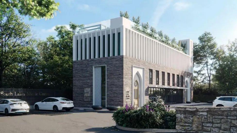 Artist's impression of how the new mosque is expected to look, with three white cars parked in a tarmaced area outside. It is a rectangular building, three-storeys high, with grey slate walls and tall, thin windows with white window frames. In front is a small area planted with shrubs and flowers, next to a stone wall.