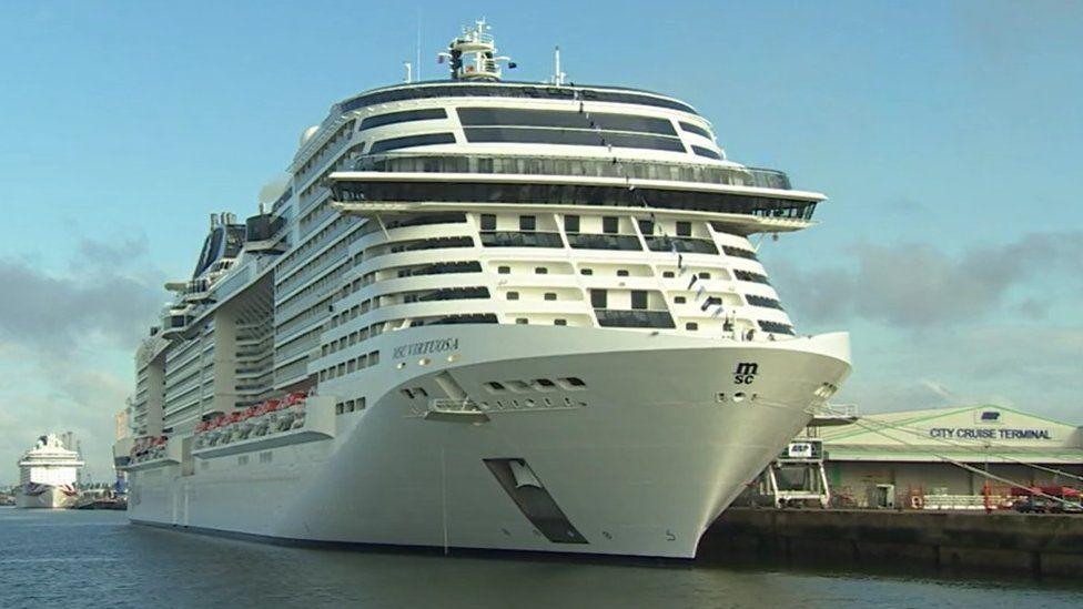 White cruise ship berthed with ropes to its left side onto the docks.
